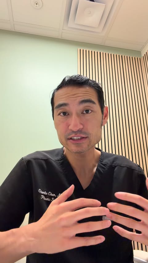 Dr. Charlie Chen in black scrubs standing before a sage wall with vertical wood slats